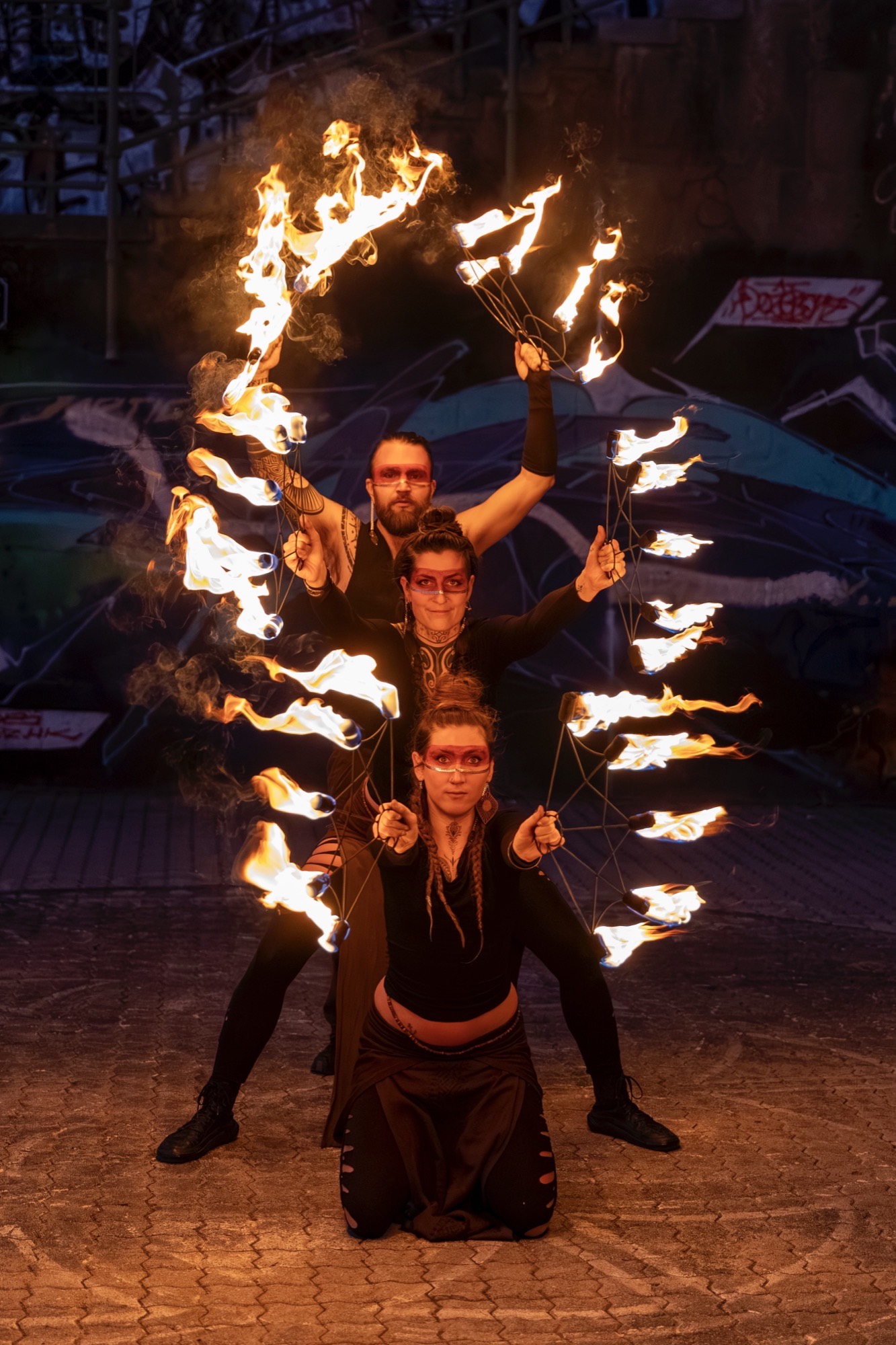 Three fire performers stacked in a row holding burning fans on pavement