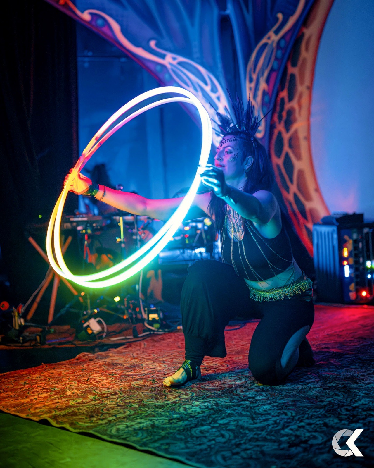 Performer kneeling with a colourful glowing LED hoop on stage