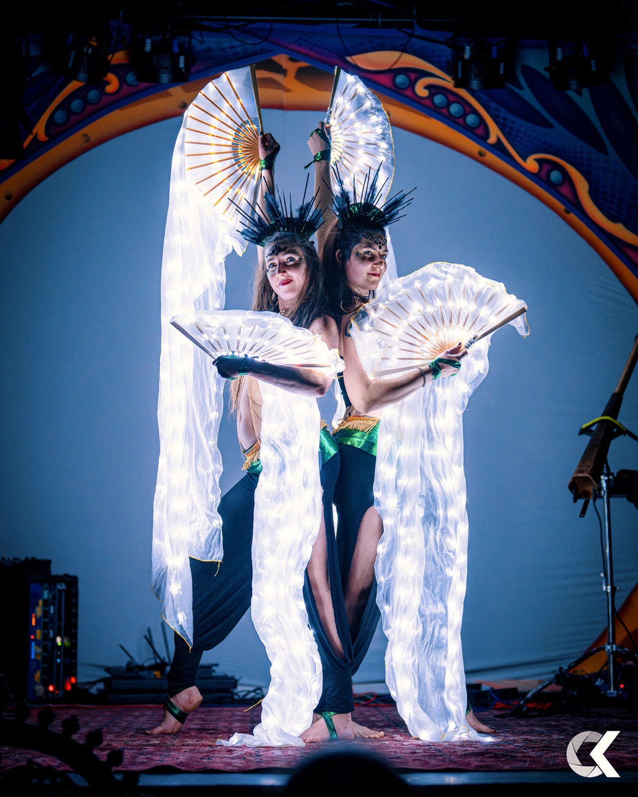 Two performers with glowing LED fans and feather crowns on stage