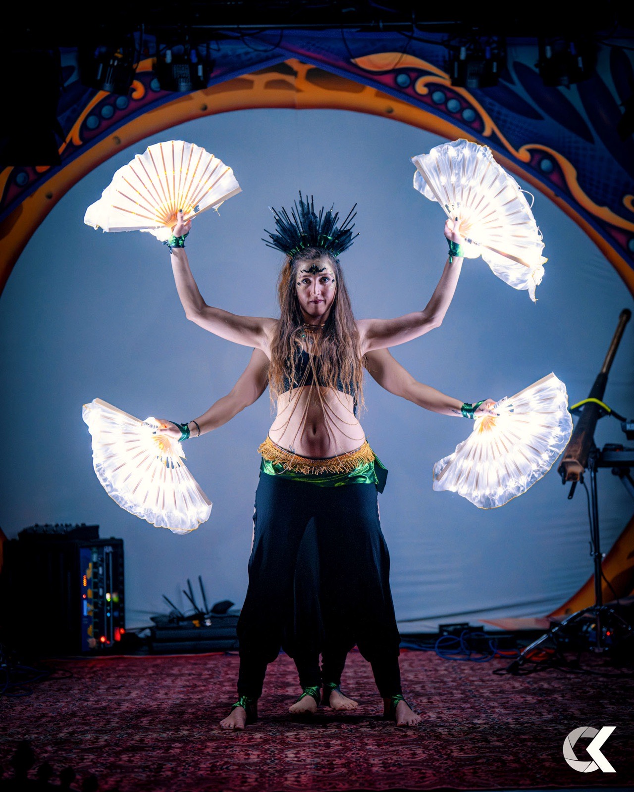 Performer with four glowing LED fans on a colourful festival stage