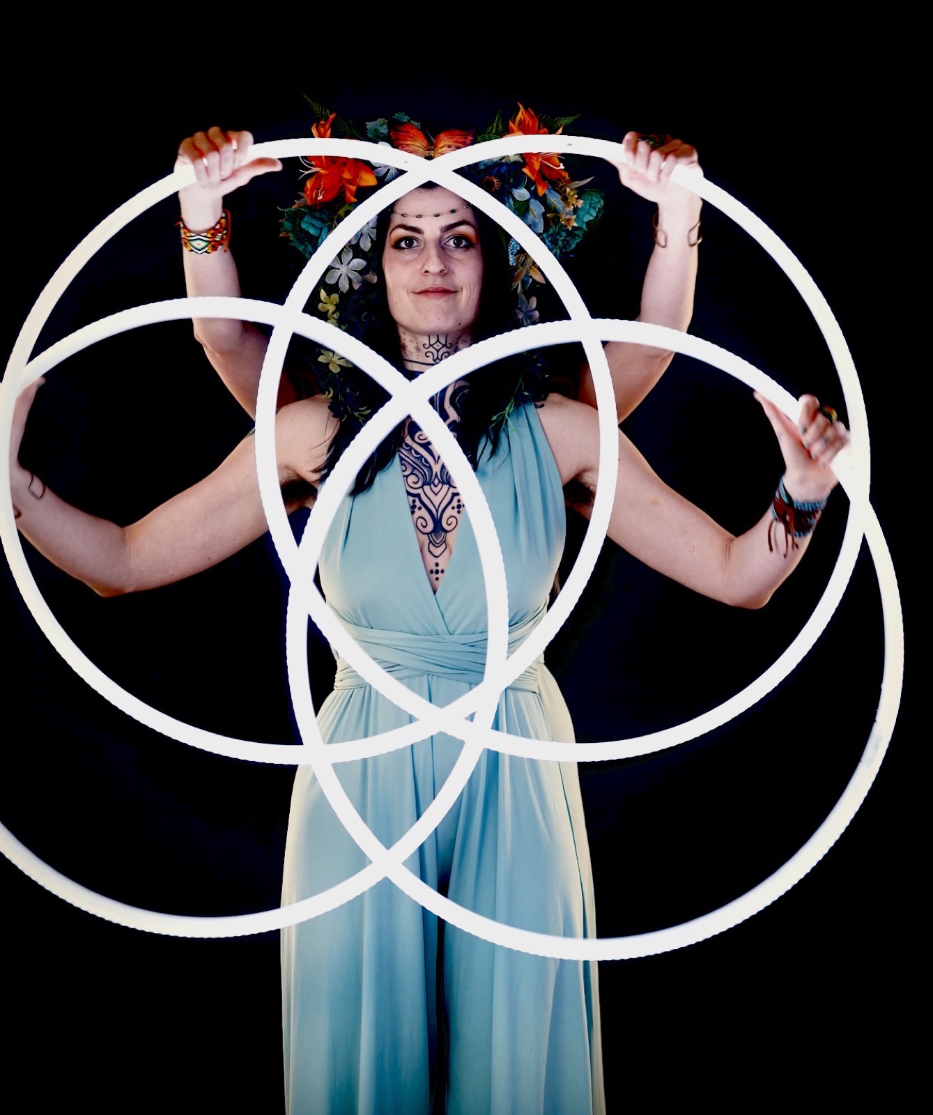 Performer with flower crown holding four white hoops on black background