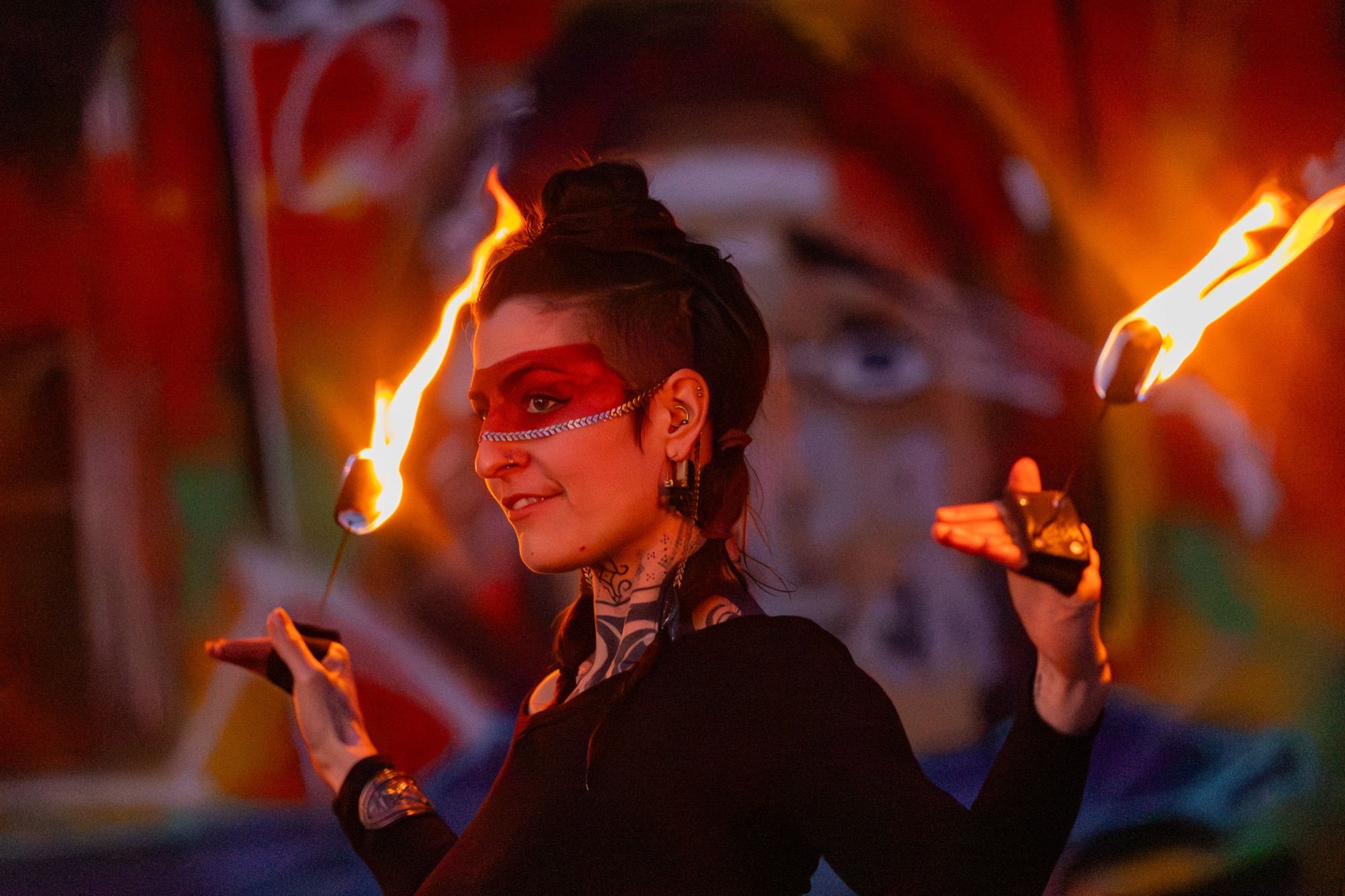 Teresa smiling with two lit fire props before a colourful graffiti wall